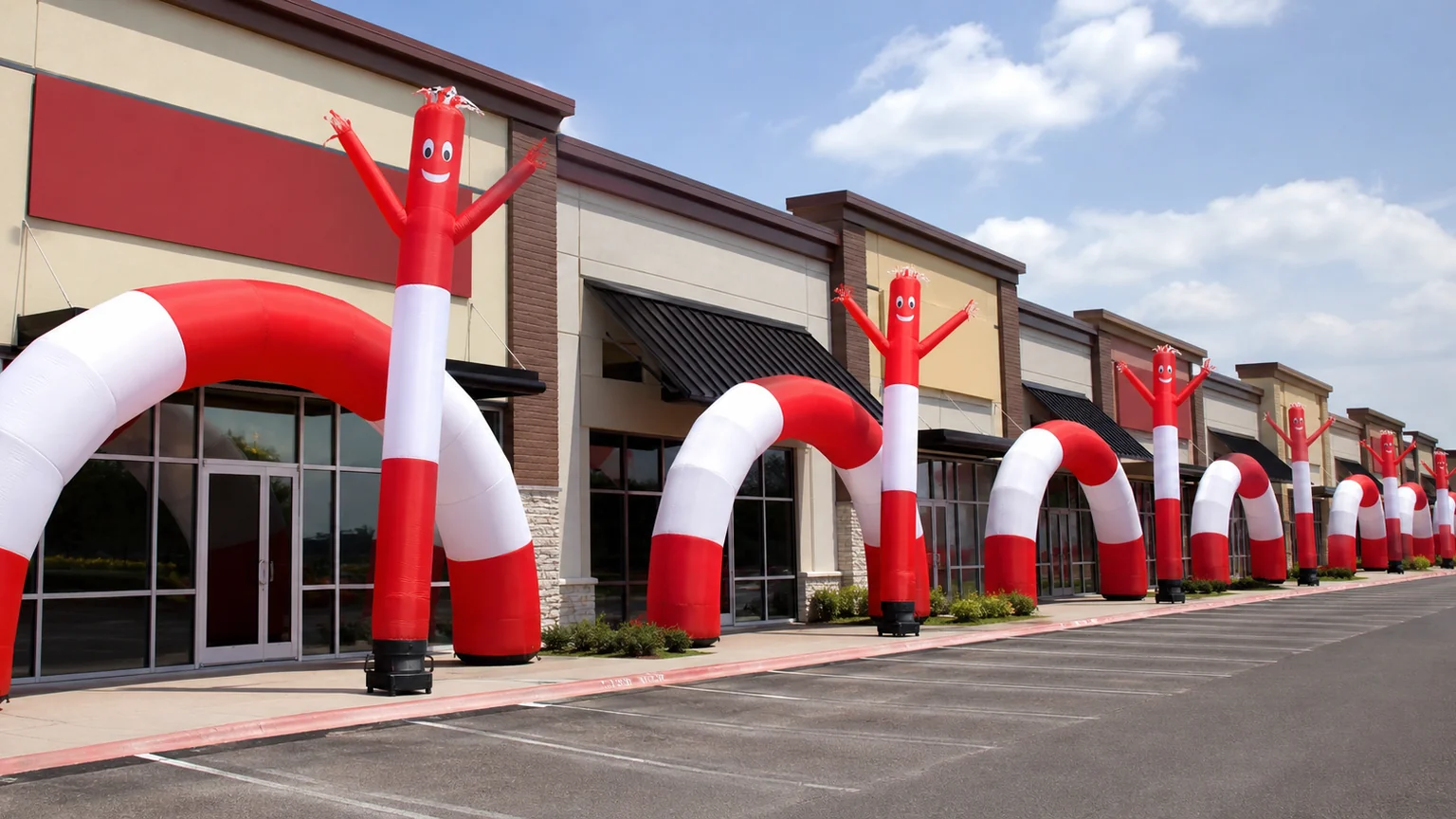 A row of identical franchise storefronts each with matching red and white inflatable air dancers and arches