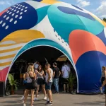 A colourful custom-printed inflatable dome tent with abstract graphics surrounded by a crowd at an event