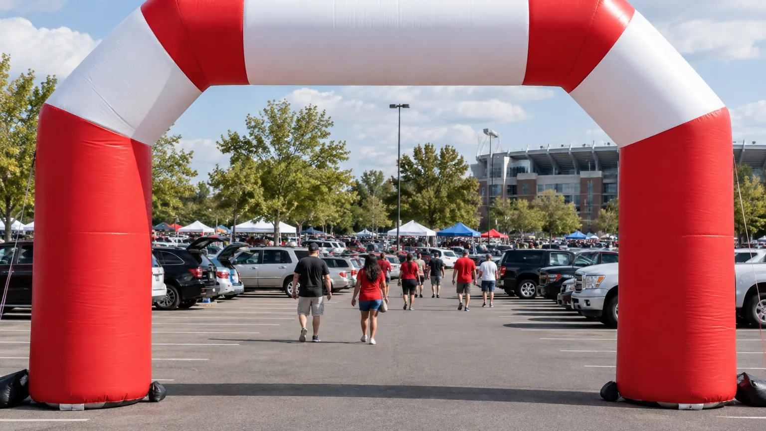 A high-contrast red and white inflatable arch framing an event entrance in a stadium parking lot with people walking through
