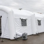 A large white multi-bay inflatable medical field tent with windows and a blower unit outdoors